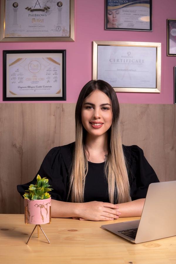 Daymaris Castillo en su estudio junto a sus certificados PhiBrows Artist y PhiBrows Craftmaster enmarcados
